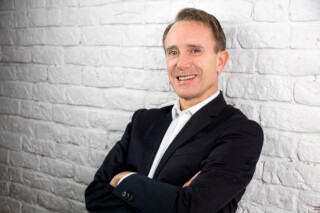 Daniel Berger, Partner Wirth Rechtsanwälte - vor weißer Steinwand - Querformat