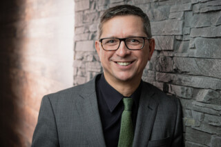 Gründer von Wirth Rechtsanwälte Norman Wirth vor einer beleuchtenden Steinwand - Querformat