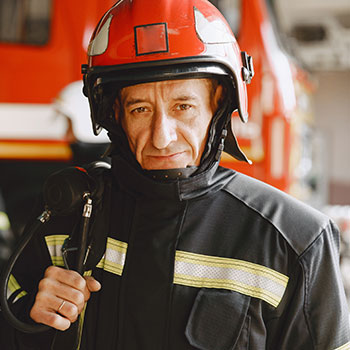 Porträt eines erfahrenen Feuerwehrmanns in Uniform und Schutzhelm vor einem Feuerwehrauto. Fallbeispiel: Unterstützung bei Problemen mit der Dienstunfähigkeitsversicherung aufgrund einer posttraumatischen Belastungsstörung (PTBS).