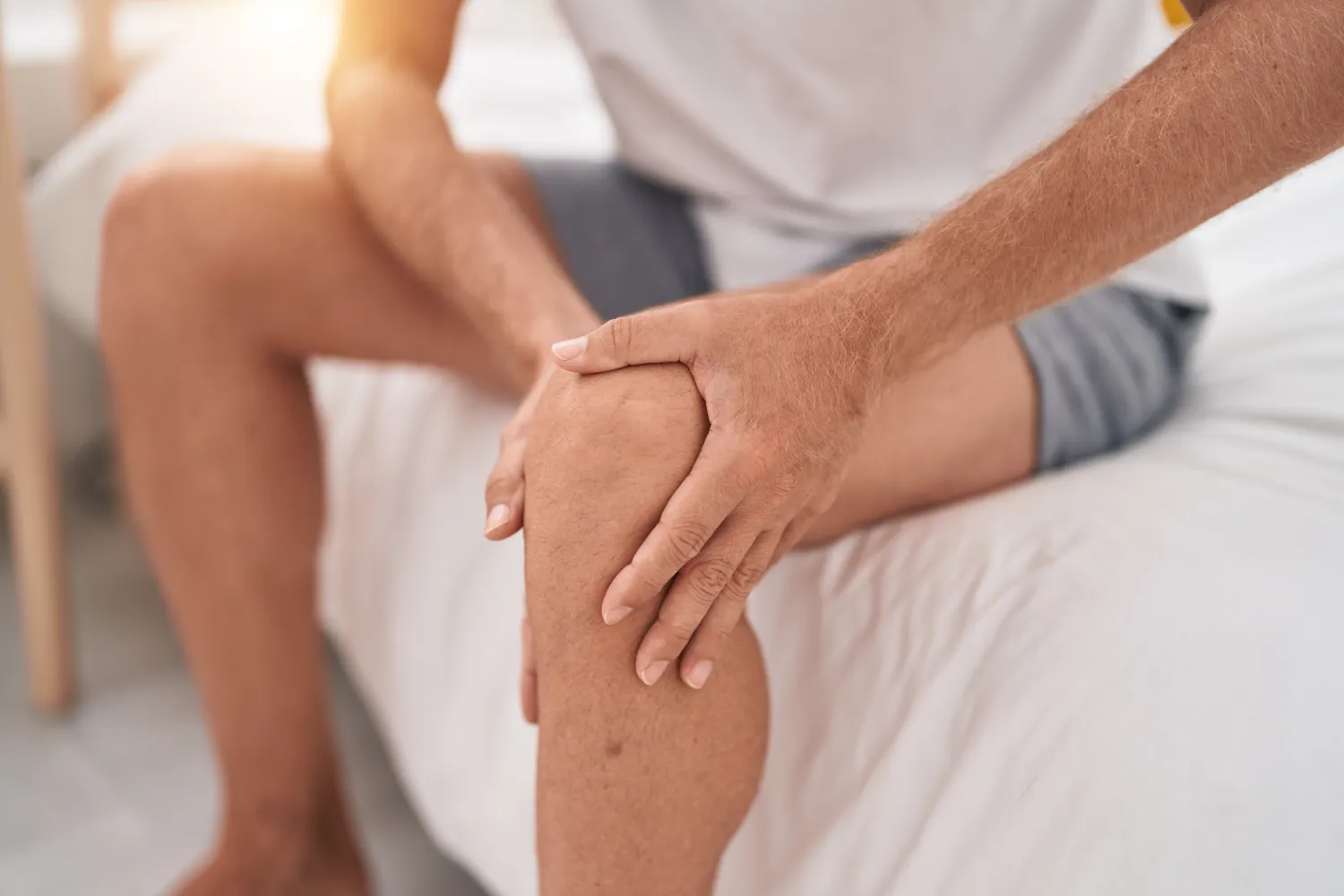 Junger Mann sitzt auf dem Bett und fasst sich ans Knie